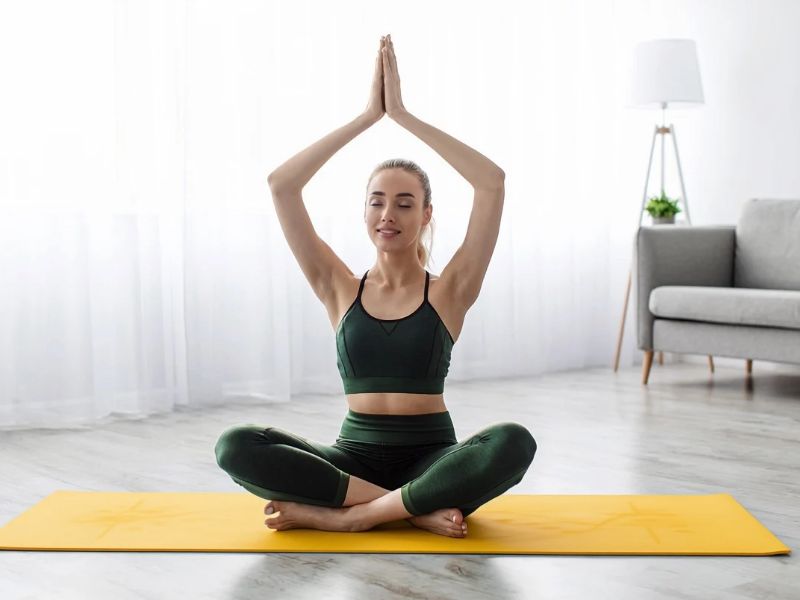 Frau sitzt im Schneidersitz auf einer Yogamatte und meditiert mit erhobenen Händen.