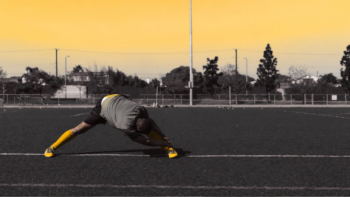 Athlet auf dem Spielfeld beim Stretching mit gelben Schuhen und Stutzen