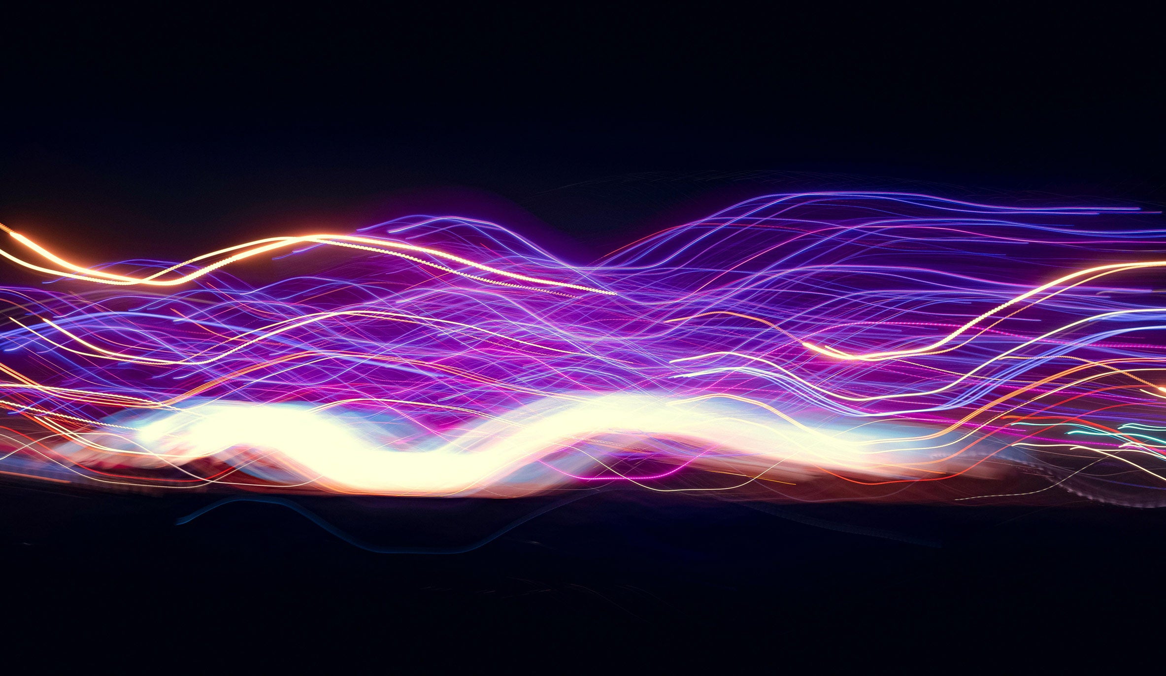 Abstrakte Lichtspuren in Violett-, Blau-, Pink- und Goldtönen verlaufen dynamisch über dunklen Hintergrund. Die fließenden Linien, die leuchtenden Farbverläufe und die futuristische Darstellung unterstützen eine moderne und energiegeladene Bildatmosphäre.